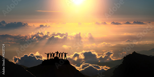 On the top of the world together. A group of people stands on a hill over the beautiful cloudscape. photo
