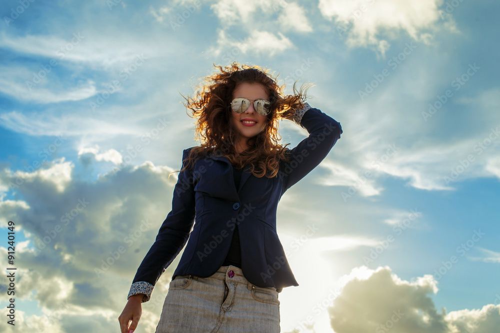 Smiling redhead girl posing over blue sky with clouds. Smiling redhead girl posing over blue sky with clouds.