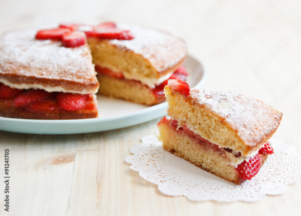 Victoria sponge cake with strawberries, jam and whipped cream with a cut out piece on a wooden table