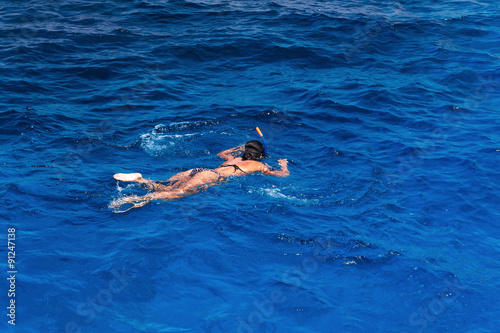 Young woman in swimsuit snorkeling in blue and transparent tropical sea