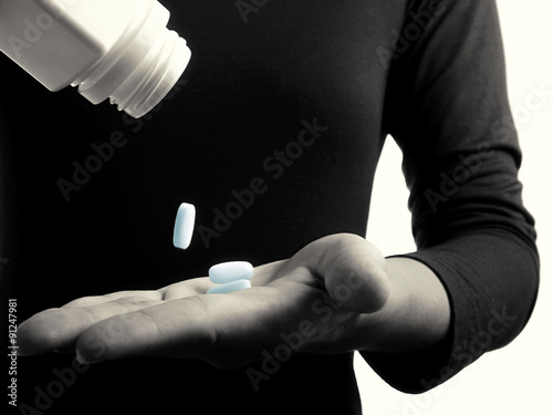 Black and white toned photo with blue  pills falling on the female hand