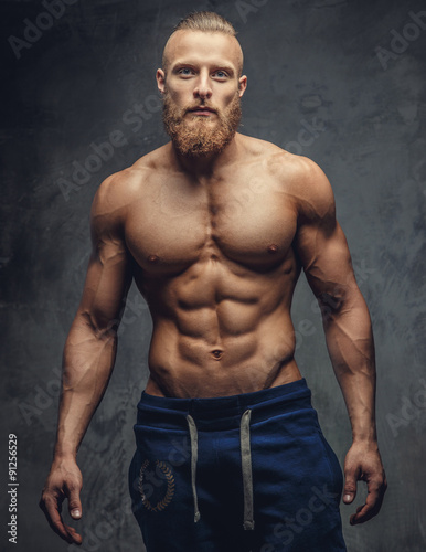 Bodybuilder with beard posing over grey background.