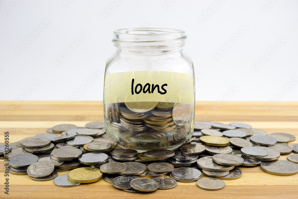 Coins in glass container with LOANS label on wooden surface against white background.Financial concept.Selective focus. Coins in glass container with LOANS label on wooden surface against white background.Financial concept.Selective focus.
