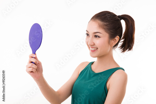 Beautiful young woman looking at herself in a hand mirror