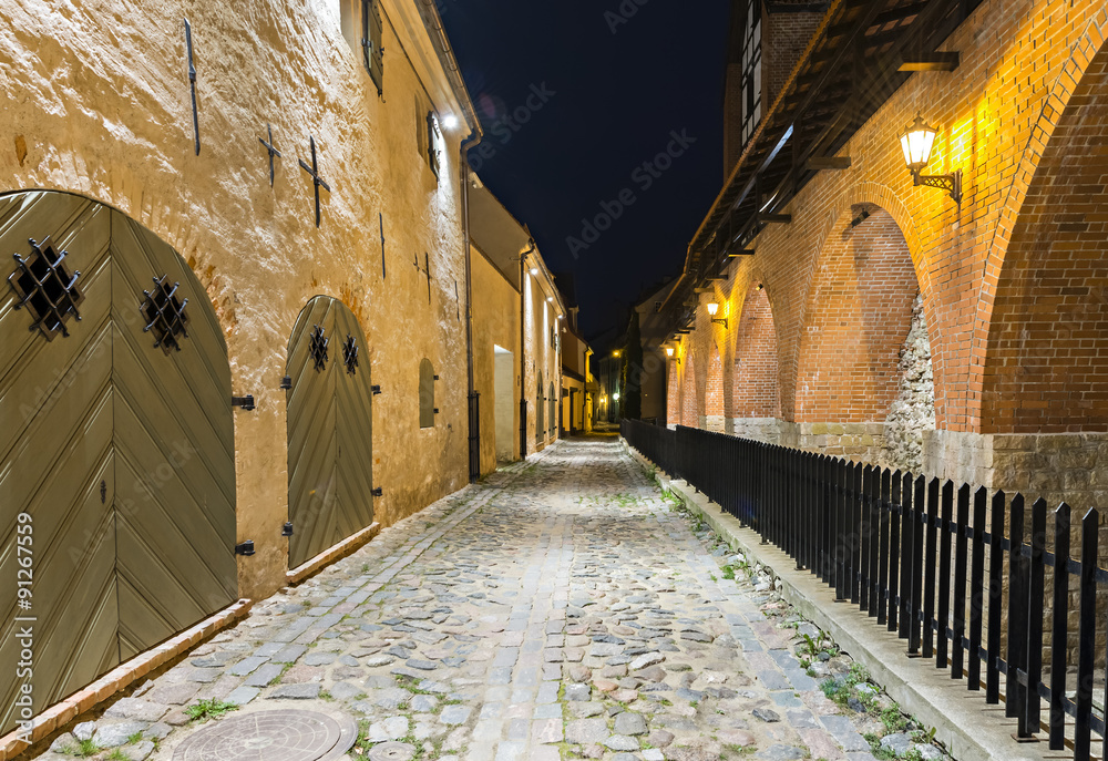 Narrow medieval street with ancient fortress wall, night photo in old Riga city, Latvia