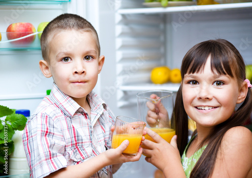 Children drink juice standing near refrigerator