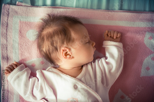 A portrait of a sweet newborn baby girl sleeping on his back wearing pajama. She is sleeping on a pink colored blanket photo