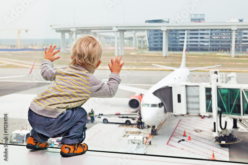 Little baby boy waiting boarding to flight in airport transit hall and looking through the window at airplane near departure gate. Active lifestyle, travel by air with child on family summer vacation photo