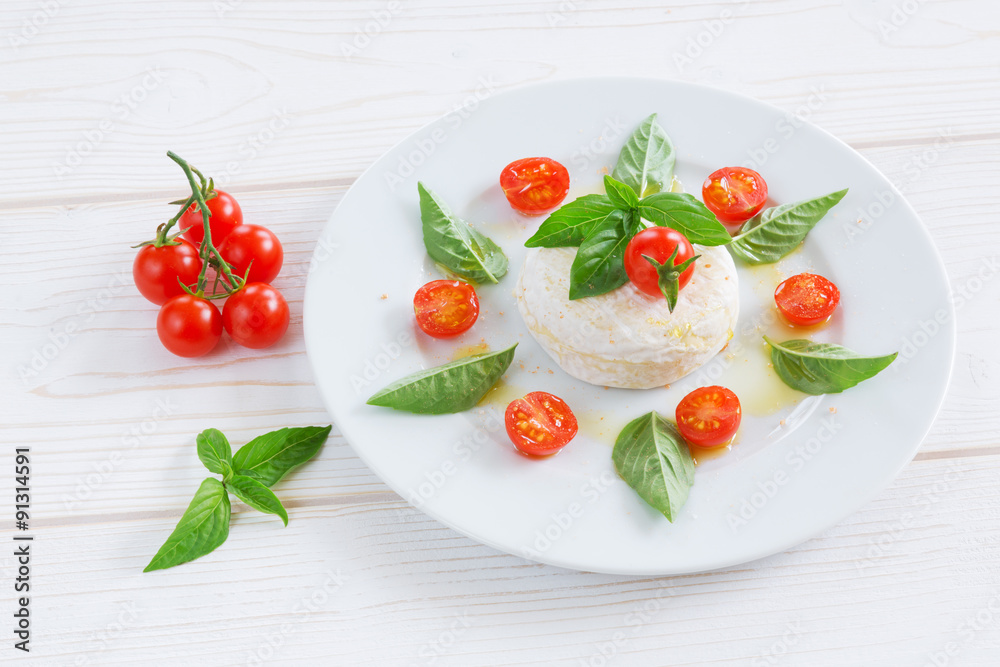 a round piece of cheese with basil and cherry tomatoes on a white plate a round piece of cheese with basil and cherry tomatoes on a white plate
