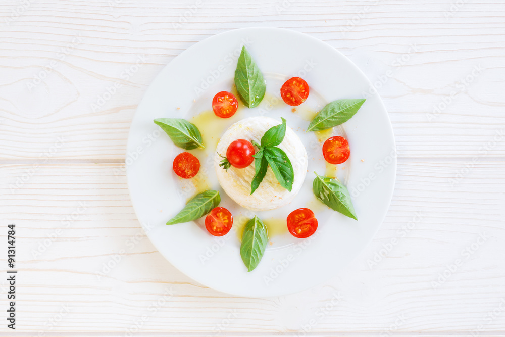 round piece of cheese with basil and cherry tomatoes on a white plate round piece of cheese with basil and cherry tomatoes on a white plate