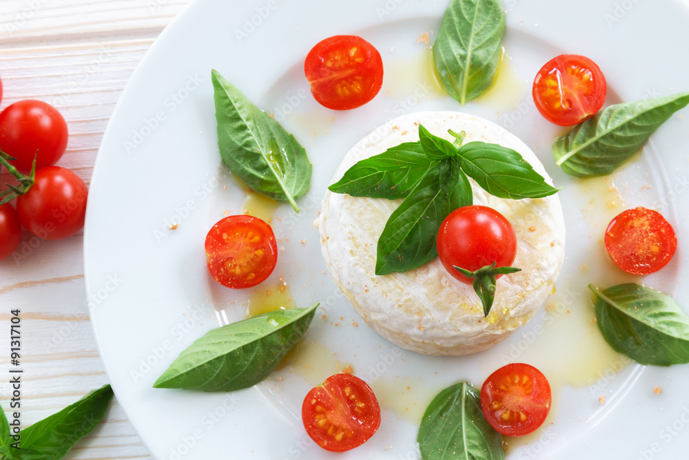 round piece of cheese with basil and cherry tomatoes on a white plate round piece of cheese with basil and cherry tomatoes on a white plate