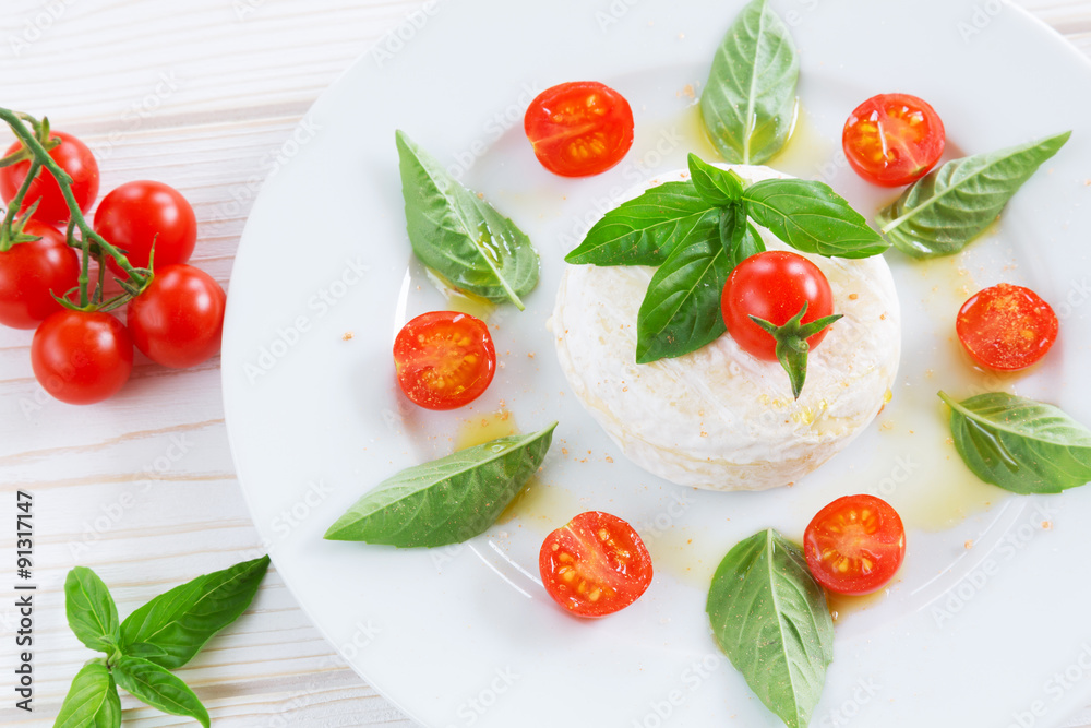 a round piece of cheese with basil and cherry tomatoes on a white plate a round piece of cheese with basil and cherry tomatoes on a white plate