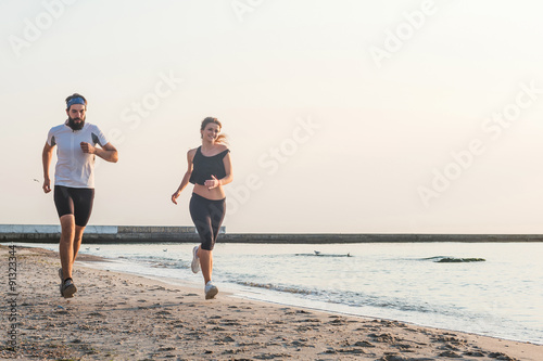 Running people - woman and man athlete runners jogging on beach. Fit young fitness couple exercising healthy lifestyle outdoors during sunrise or sunset