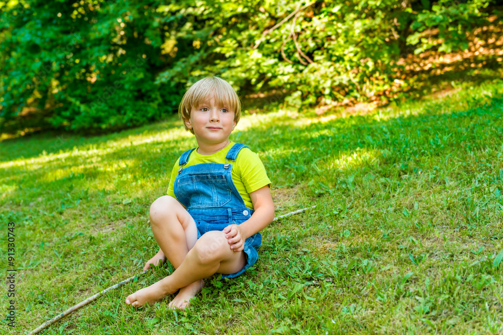 Little boy playing outdoors on a nice sunny summer day wearing denim overalls