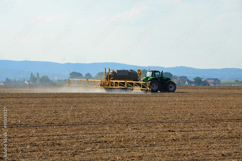 Fototapeta premium Plowed field with a tractor treating the soil