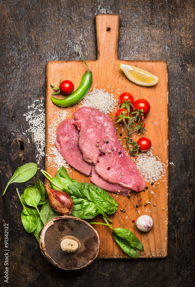 turkey steak on a cutting board with mushrooms and green peppers tomatoes and lemon garlic on wooden rustic background top view