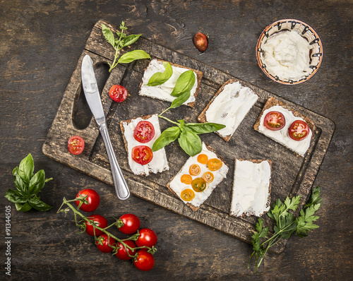 cheese sandwiches with tomatoes on a branch and herbs on a cutting board with a knife on wooden rustic background top view