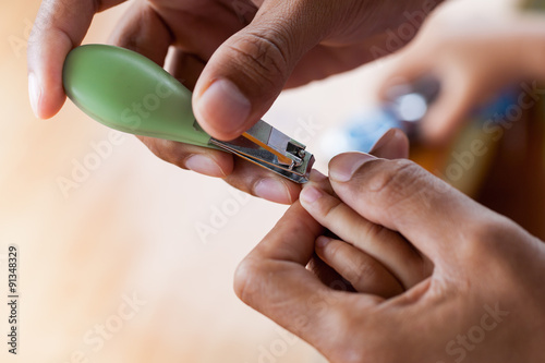 Father cutting fingernails for his baby on wooden table backgrou