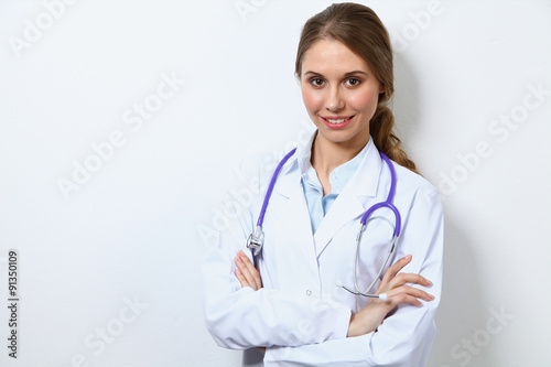 Friendly smiling young female doctor, standing near wall