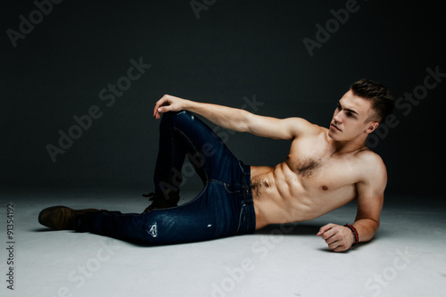Young fashion topless man lying on the floor isolated on dark background