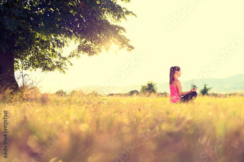 Young athletic woman practicing yoga on a meadow at sunset, image with lens flare © andreaobzerova