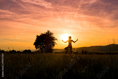 Young athletic woman practicing yoga on a meadow at sunset, silhouette