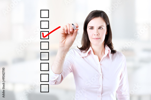 Young business woman checking on checklist box. Office background.