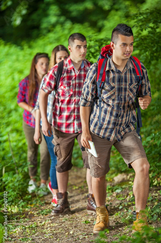 Group of young friends hiking in forest with backpacks and maps exploring nature