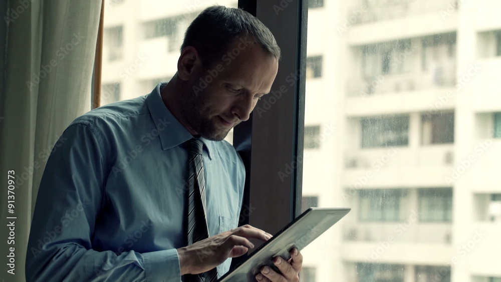 Young businessman using tablet computer while standing by window at home Young businessman using tablet computer while standing by window at home