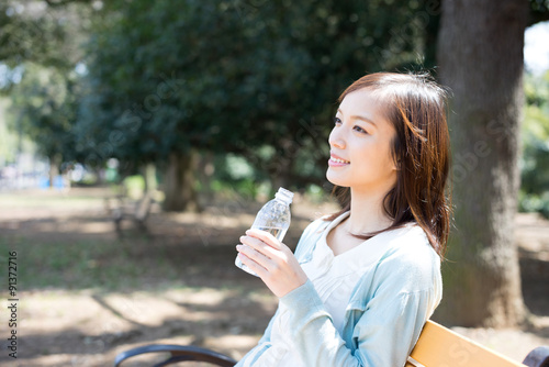 公園のベンチで水を飲む女性