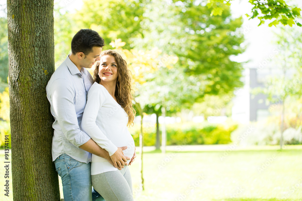 Naklejka premium Happy and young pregnant couple in park in summer