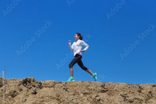 young woman running on mountain trail with blue sky background