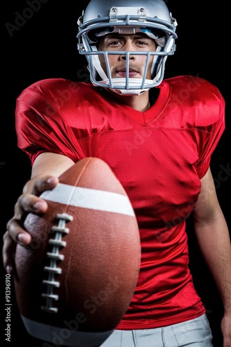 Portrait of serious American football player showing ball