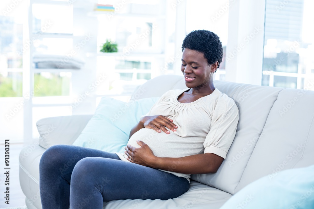 Pregnant woman touching her belly while sitting at home