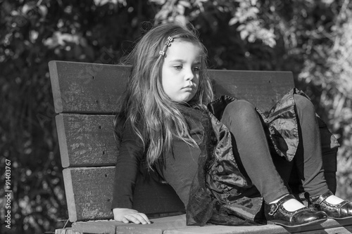 tired or bored little girl sitting on a bench, black and white photo