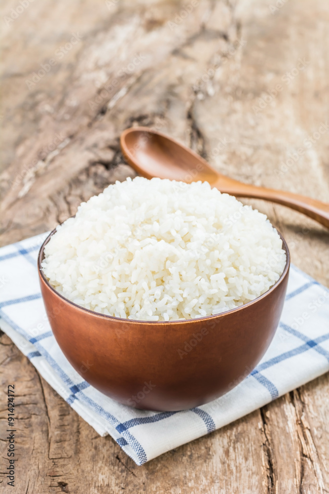 Cooked rice in bowl with spoon and dishcloth on old wooden table Cooked rice in bowl with spoon and dishcloth on old wooden table