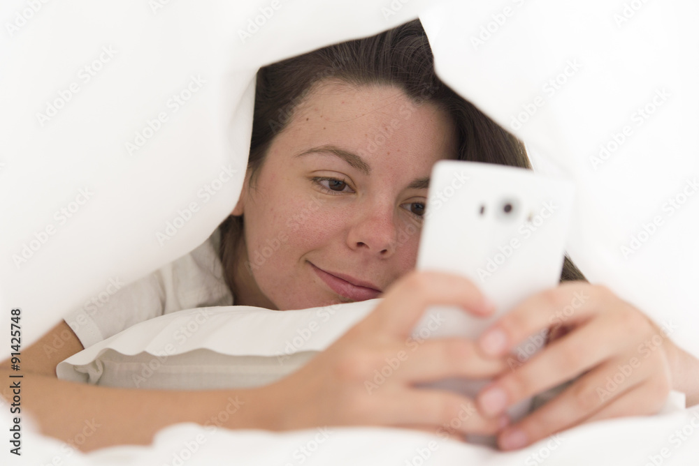 Relaxed young woman with mobile phone lying in bed at home Relaxed young woman with mobile phone lying in bed at home