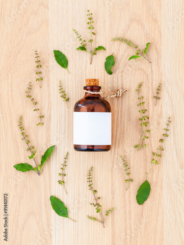 Bottle of essential oil with holy basil leaf and flower on woode