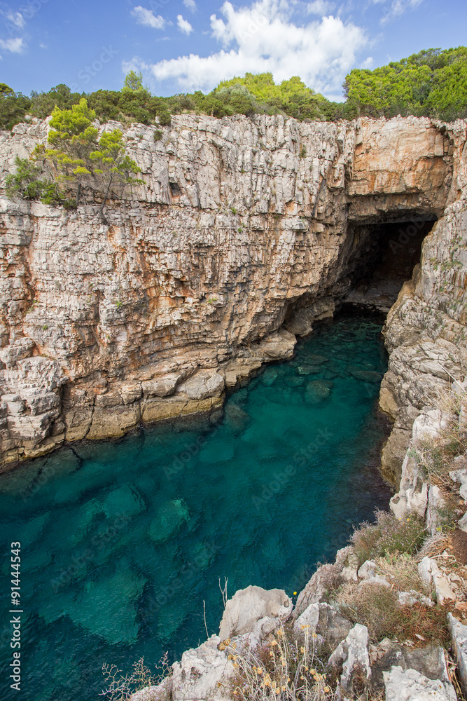 Empty sea cave, shallow water and steep and rugged cliff at the Lokrum Island in Croatia.