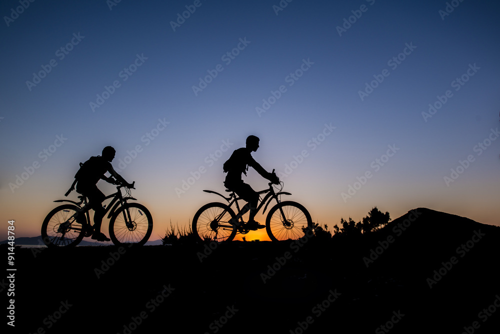 Obraz premium Silhouette of a men on mountain bike at sunset 