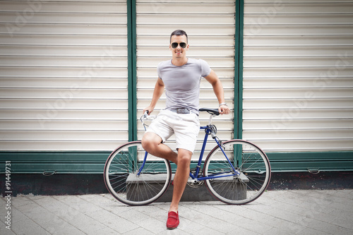 Handsome young man leaning on his bicycle and smiling to camera
