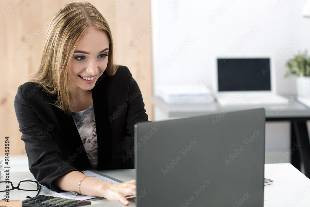 Young smiling business woman working at laptop in the office Young smiling business woman working at laptop in the office