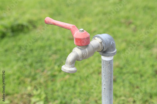 close up of water faucet with green grass background - Selective