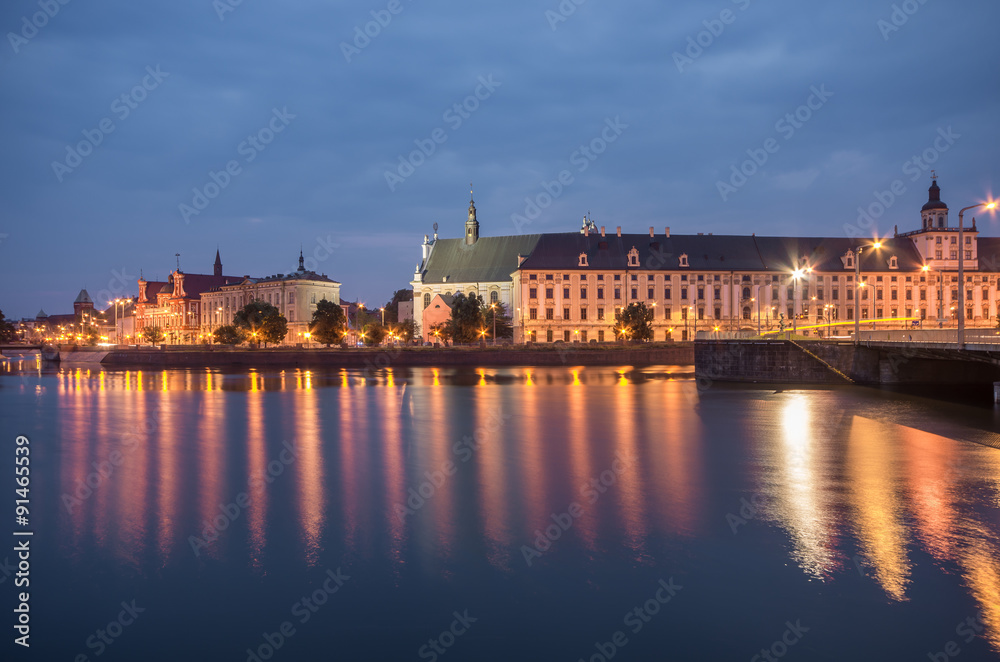 Fototapeta premium Odra river waterfront in Wroclaw, Poland, with university church and main university building, in early morning, seen from Malt Island (Wyspa Slodowa)