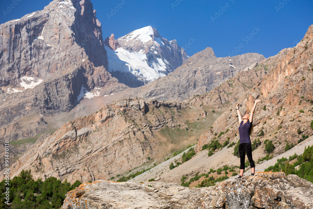 Morning Warming Up of Female Climber Attractive Young Woman Staying in Worshiping Posture  with Arms Raised Up  on Top of High Rock in Mountains
