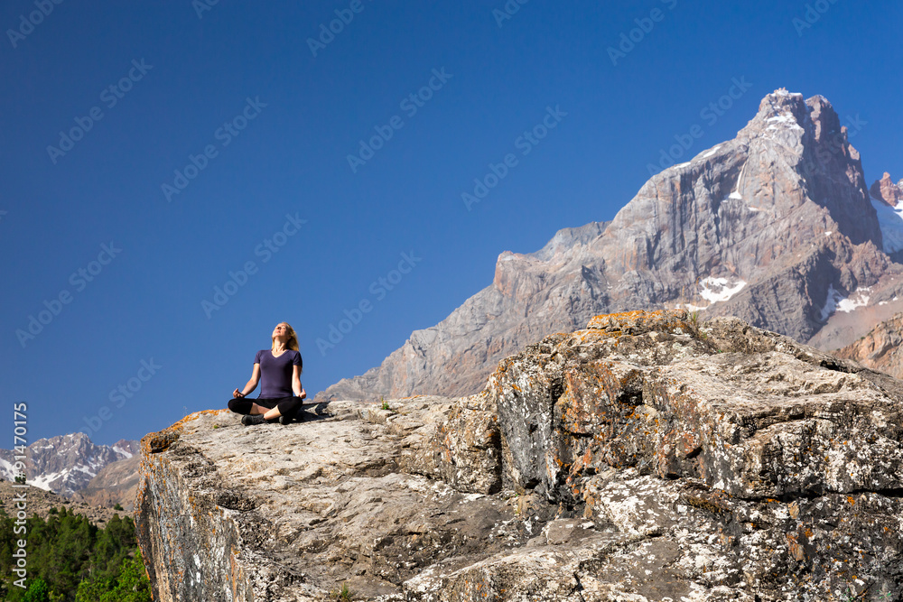 Young woman doing exercise Female Rock Climber Sitting in Yoga Zen Mediation Pose to Stretch Body Mountain Panoramic Landscape Outdoor Sunny Sky Peaks