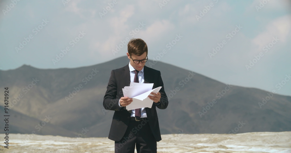 Businessman looking through documents and throwing them into air in desert Businessman looking through documents and throwing them into air in desert