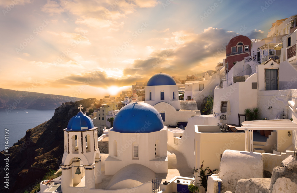 Naklejka premium Traditional white architecture in Oia Santorini, illuminated by a beautiful sunset in Greece - Europe