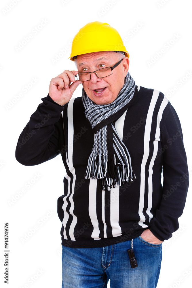 Emotional old senior man in sweater, jeans, scarf, glasses, wearing yellow construction hat. Holding and fixing his glasses with the finger with an opened mouth. Isolated, plain white background