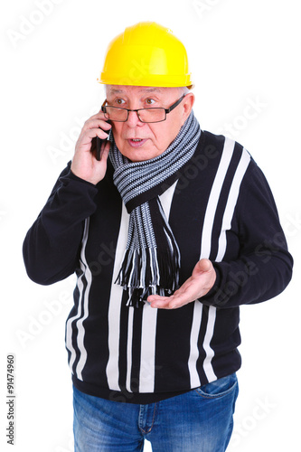 Emotional portrait of old senior man construction worker talking on cell phone in dressed helmet, jeans, scarf and glasses, holding smartphone in hand, Isolated, Human emotions and facial expressions